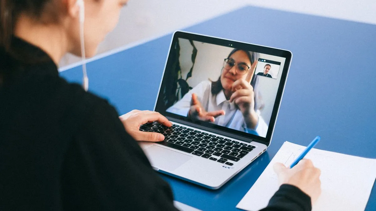 Frau im Videogespräch am Laptop, macht sich währenddessen Notizen auf einem Block